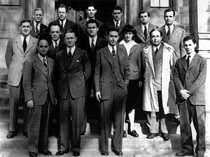 A group of people in suits standing in three rows on the steps in front of a stone building