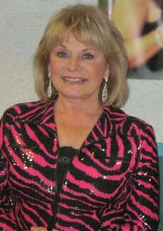 A woman with long grey hair wearing a pink and black striped jacket