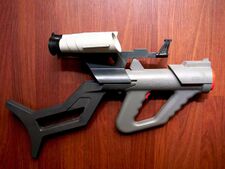 Plastic, gray toy gun with orange highlights and attached black shoulder stock and white scopes.