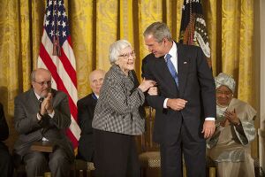 A color photograph of Harper Lee smiling and speaking to President George W. Bush while other seated Medal of Freedom recipients look on